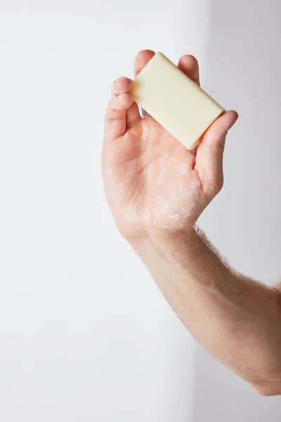 Vista parcial del hombre sosteniendo jabón en la mano sobre fondo gris - foto de stock