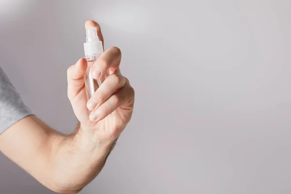 Vista ritagliata di uomo tenendo mano igienizzante in bottiglia spray su sfondo grigio — Foto stock