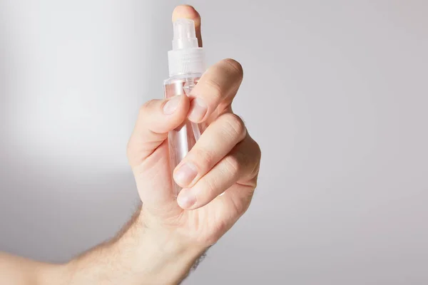 Vue recadrée de l'homme tenant un désinfectant pour les mains dans un flacon pulvérisateur sur fond gris — Photo de stock