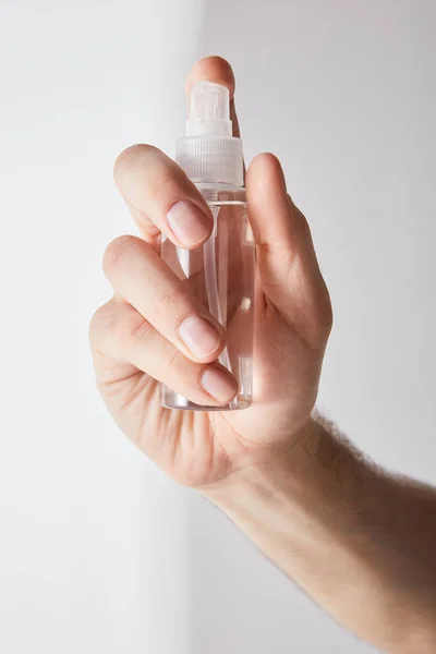 Vista cortada do homem segurando higienizador de mão em frasco de spray em fundo cinza — Fotografia de Stock