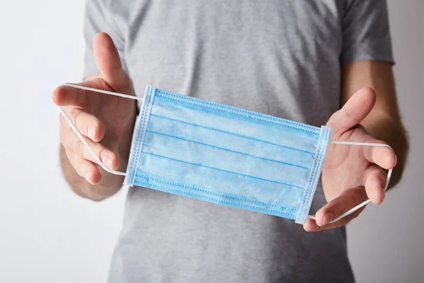 Cropped view of man holding  medical mask on grey background — Stock Photo