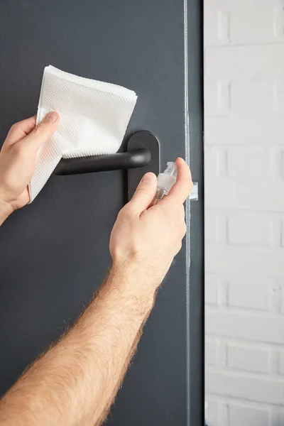 Vista parcial del hombre desinfectando la manija de la puerta de metal con antiséptico y servilleta - foto de stock