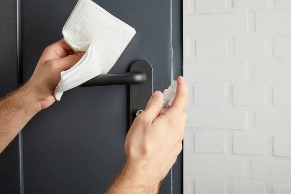 Vista parcial del hombre desinfectando la manija de la puerta de metal con antiséptico y servilleta - foto de stock