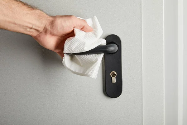 Partial view of man cleaning metal door handle with napkin — Stock Photo