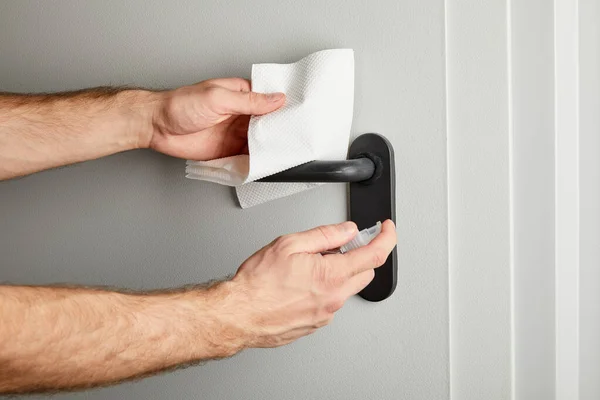 Partial view of man disinfecting door handle with antiseptic and napkin — Stock Photo