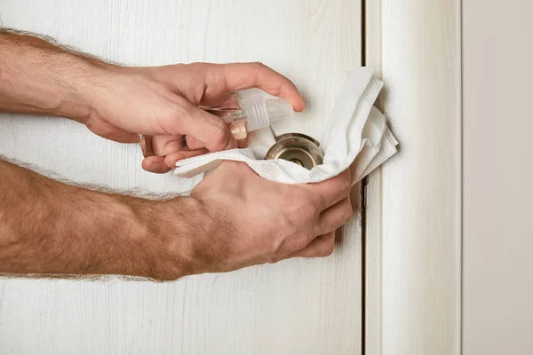 Vista recortada del hombre desinfectando la manija de la puerta con antiséptico y servilleta - foto de stock