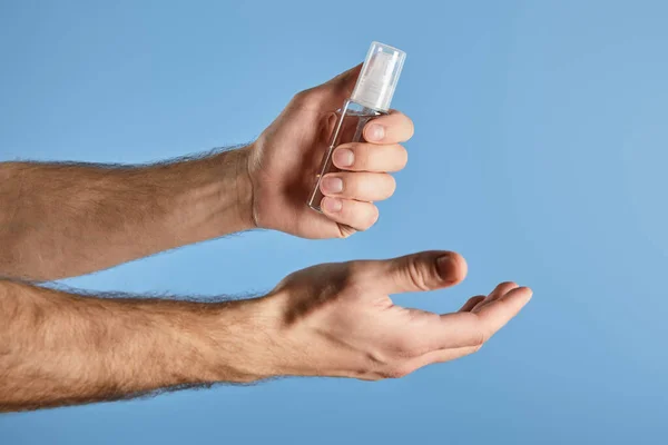 Vista ritagliata di uomo tenendo mano igienizzante in bottiglia spray isolato su blu — Foto stock