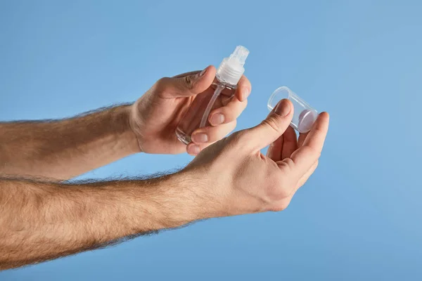 Vista recortada del hombre que sostiene el desinfectante de la mano en botella del aerosol aislada en azul - foto de stock
