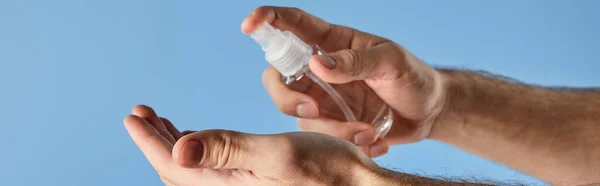 Vista recortada del hombre usando desinfectante de manos en botella de spray aislado en azul, plano panorámico - foto de stock