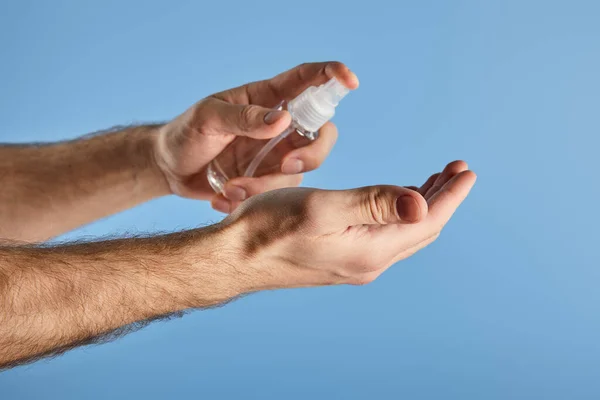 Cropped view of man using hand sanitizer in spray bottle isolated on blue — Stock Photo