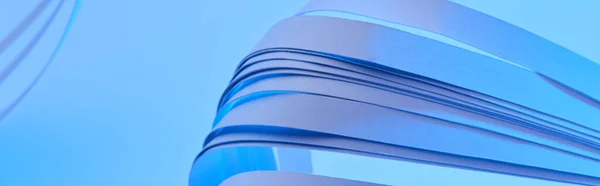 Close up view of curved colorful paper stripes on neon blue background, panoramic shot — Stock Photo