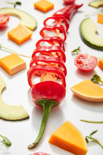 Selective focus of microgreens, cut chili pepper, pumpkin and cherry tomato with avocado slices on white — Stock Photo