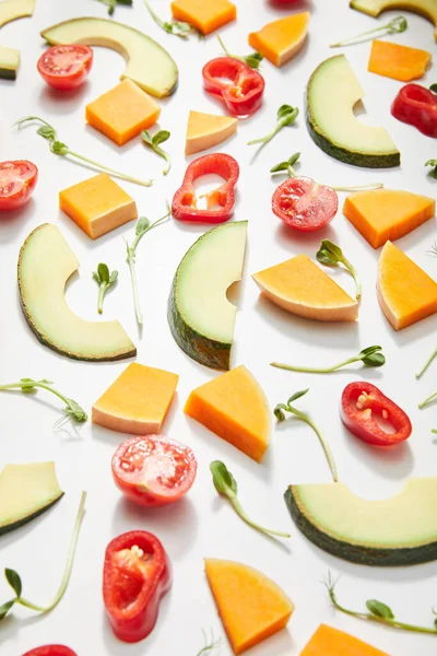 Vista en ángulo alto de microgreens, verduras frescas cortadas y rodajas de aguacate maduras en blanco - foto de stock