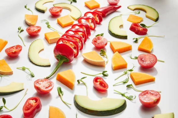 Vista en ángulo alto de microgreens, ingredientes cortados y rodajas de aguacate maduras sobre fondo blanco - foto de stock