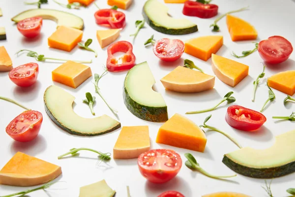 Foco seletivo de microverdes, corte tomates cereja maduros, pimenta, abóbora e fatias de abacate no fundo branco — Fotografia de Stock