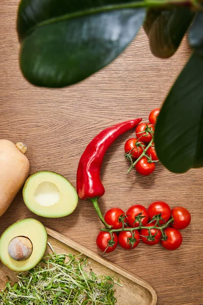 Selective focus of green leaves, whole vegetables, avocado halves and microgreens on cutting board on wooden background — Stock Photo