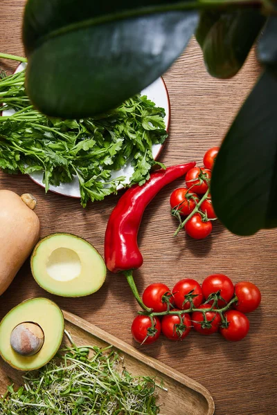 Selective focus of green leaves, vegetables, avocado halves, greenery and microgreens on cutting board on wooden background — Stock Photo