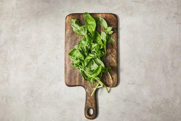 Vue du dessus de la planche à découper avec feuilles de basilic sur fond gris — Photo de stock