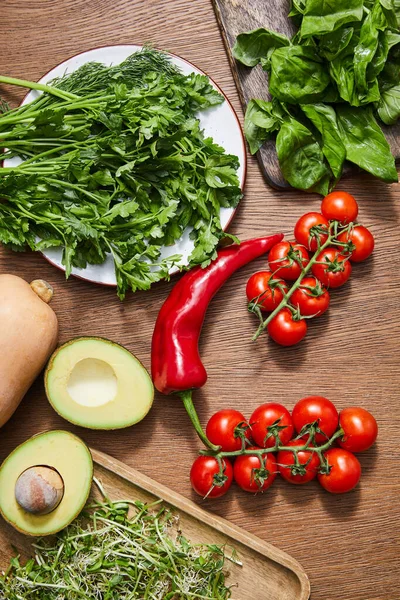 Vista superior de verduras, mitades de aguacate, vegetación, microgreens y hojas de albahaca en tablas de cortar sobre fondo de madera - foto de stock