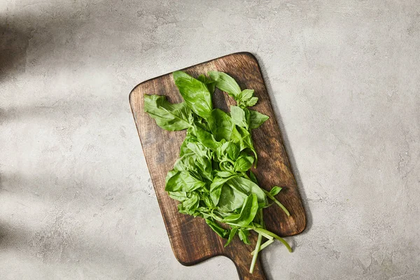 Vue du dessus de la planche à découper avec feuilles de basilic sur fond gris — Photo de stock