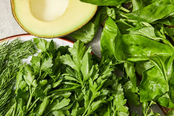 Vista superior de vegetación, hojas de albahaca y mitad aguacate sobre fondo gris - foto de stock