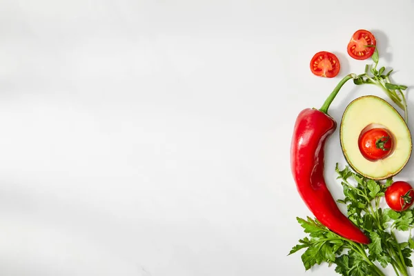 Ansicht von Petersilie, Chilischote, Kirschtomaten und Avocado zur Hälfte auf weißem Hintergrund — Stockfoto