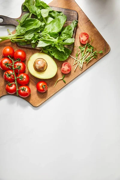 Top view of basil leaves, cherry tomatoes, avocado half and microgreens on cutting boards on white background — Stock Photo