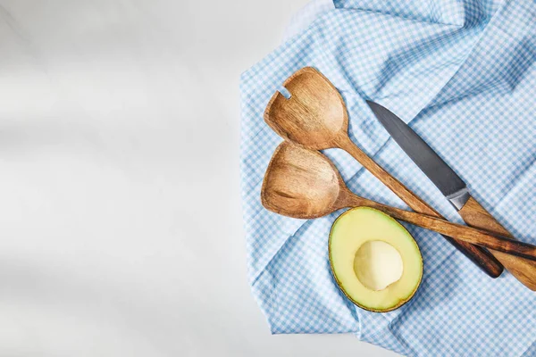 Vista superior de espátulas, cuchillo y aguacate medio sobre tela a cuadros sobre fondo blanco - foto de stock