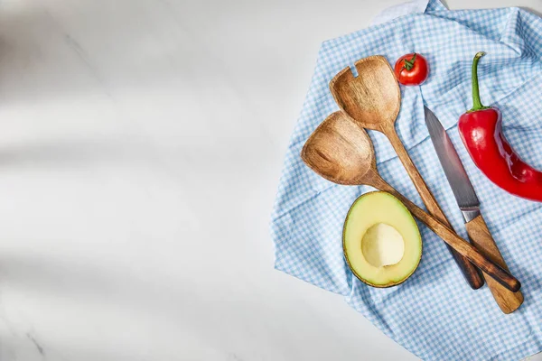 Vista superior de espátulas, cuchillo, tomate cherry, chile y aguacate medio sobre tela a cuadros sobre fondo blanco - foto de stock