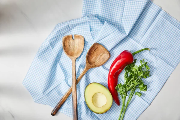 Top view of spatulas, parsley, chili pepper and avocado half on plaid cloth on white background — Stock Photo