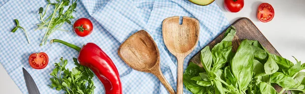 Vue de dessus des légumes, de la verdure et des spatules sur tissu près du basilic sur planche à découper sur blanc, vue panoramique — Photo de stock