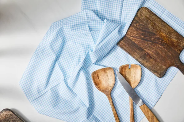 Vue du dessus des spatules, couteau et planche à découper sur toile à carreaux sur fond blanc — Photo de stock