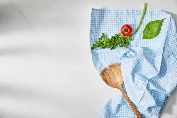 Vista dall'alto di foglia di basilico, prezzemolo, pomodoro ciliegia e spatola su tessuto plaid su fondo bianco — Foto stock
