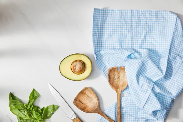 Top view of basil, knife, spatulas and avocado half near plaid cloth on white background — Stock Photo
