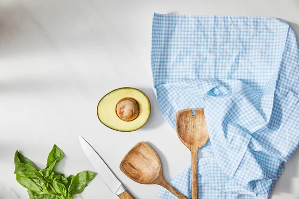 Vue de dessus du basilic, couteau, spatules et avocat demi près de tissu à carreaux sur fond blanc — Photo de stock