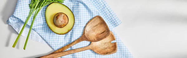 Top view of parsley, spatulas and avocado half on plaid cloth on white background, panoramic shot — Stock Photo