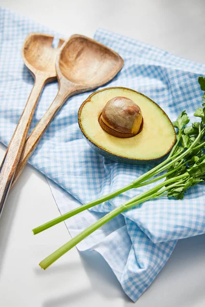 Selektiver Fokus von Petersilie, Spachteln und Avocadohälfte auf kariertem Tuch auf weißem Hintergrund — Stockfoto