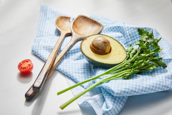 Selektiver Fokus von Petersilie, Spachteln und Avocadohälfte auf kariertem Tuch in der Nähe von Kirschtomaten auf weißem Hintergrund — Stockfoto