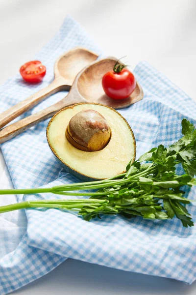 Focus selettivo di prezzemolo, spatole, pomodorini ciliegia e avocado metà su un panno a quadri su sfondo bianco — Foto stock