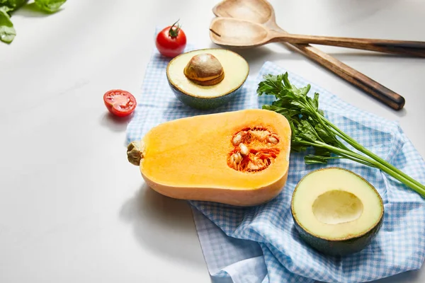 Vista ad alto angolo di verdure, verde e avocado metà su stoffa vicino spatole su sfondo bianco — Foto stock