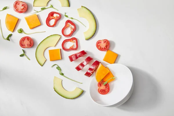 Вид зверху миски з мікрогрін, нарізані овочі та скибочки авокадо на білому тлі — стокове фото