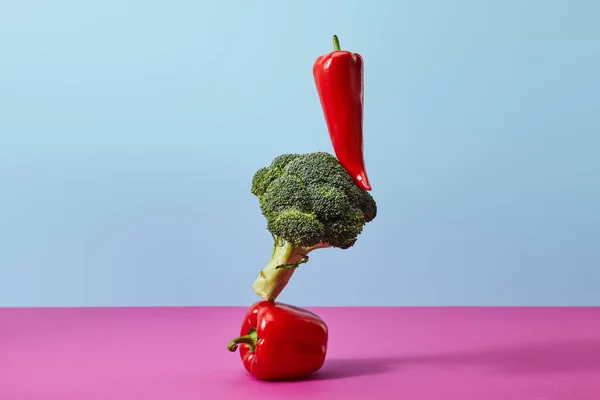 Ripe broccoli, chili and bell peppers on blue and pink — Stock Photo