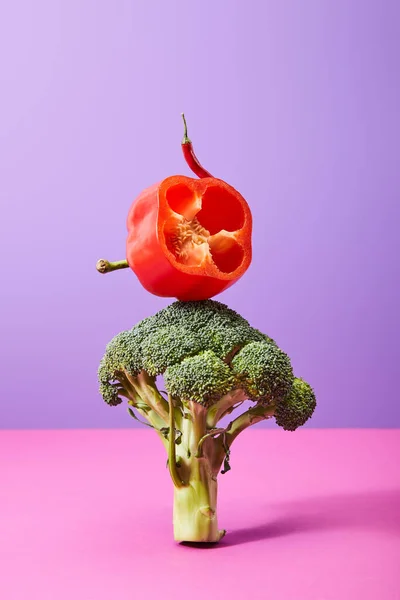 Chili pepper and fresh half of bell pepper on broccoli on purple and pink — Stock Photo