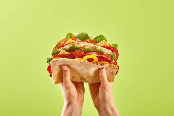 Cropped view of woman holding fresh sandwich with salami, pita, vegetables and cheese isolated on green — Stock Photo