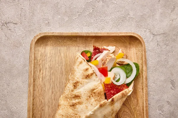 Vue du dessus du burrito frais avec poulet et légumes à bord sur fond gris béton — Photo de stock