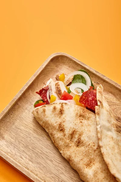 Свежий буррито с курицей и овощами на борту на оранжевом фоне — стоковое фото
