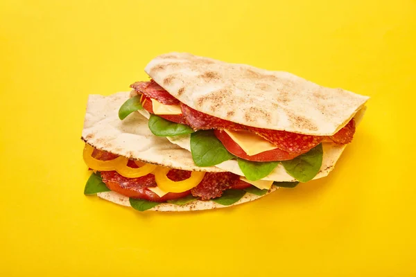 Fresh sandwiches with salami, pita, vegetables and cheese on yellow background — Stock Photo