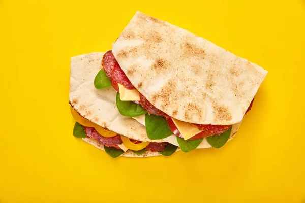 Sanduíches frescos com salame, pita, legumes e queijo em fundo amarelo — Fotografia de Stock