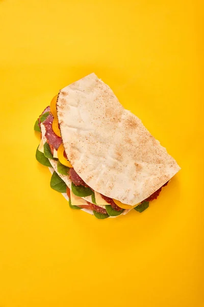 Vista superior de sanduíche fresco com salame, pita, legumes e queijo no fundo amarelo — Fotografia de Stock