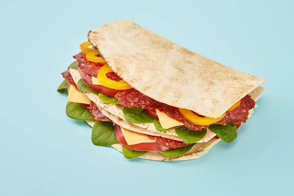 Sándwich fresco con salami, pita, verduras y queso sobre fondo azul - foto de stock